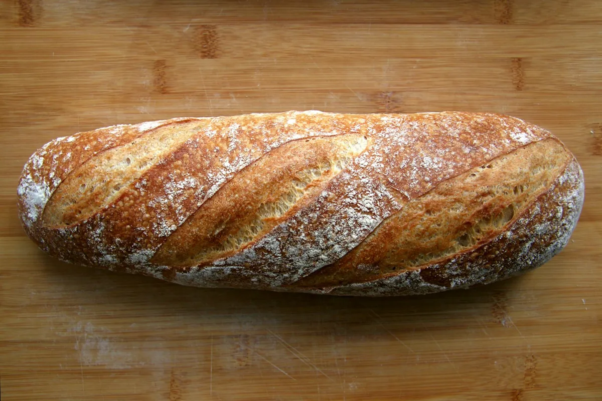 Barra de pan de masa madre con la corteza enharinada sobre una tabla de madera