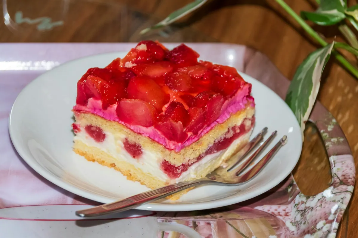 Porción de tarta de fresas con bizcocho y nata en un plato blanco con tenedor